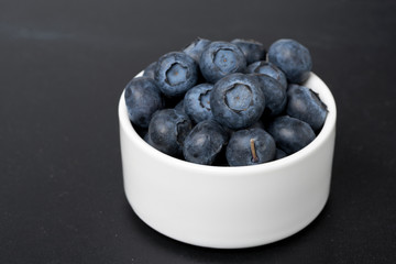 white bowl with blueberries on a black background, close-up