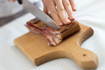Woman's hands cutting bacon into strips, close up