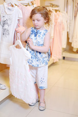 Little girl considers white dress in store with children clothes