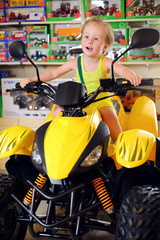 Little cute boy in yellow sits on toy quad bike in store