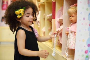 Little smiling girl touches dummy of toy doll in children store.