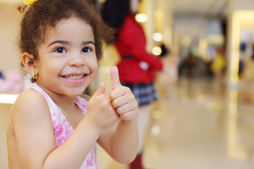 Little pretty girl smiles and thumbs up in children store