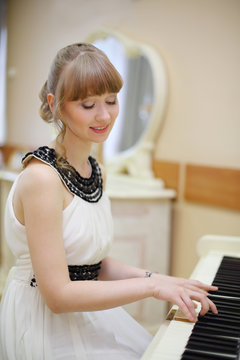 Beautiful smiling girl in white dress plays white piano