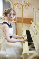 Beautiful focused girl in white dress plays white piano