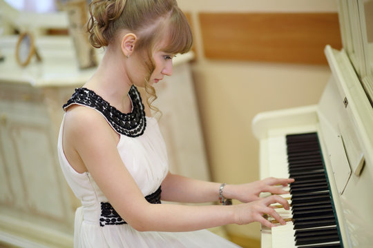 Beautiful focused girl in white dress plays white piano