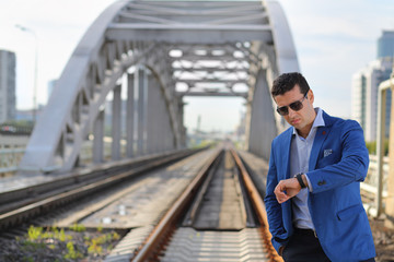 Handsome man in blue jacket and sunglasses stands on railroad