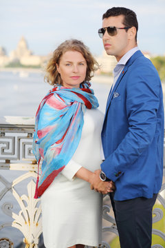 Stylish man in jacket and pregnant woman stand on bridge