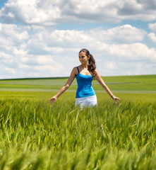 Happy carefree young woman in a green wheat field