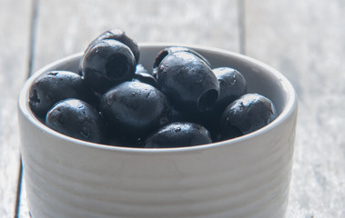 Black olives close up in bowl on wooden background