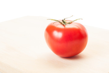 One red tomato on wooden plate and white background.