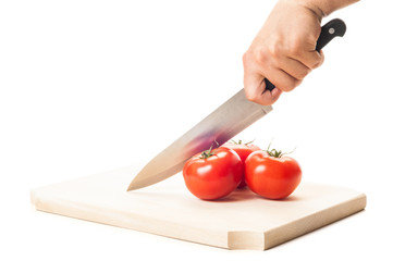 Hand holding a big knife, three tomatoes and wooden board.