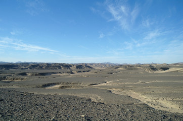 Egyptian desert covered by black stones and blue sky.