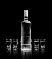 Bottle and glasses of vodka standing isolated on black