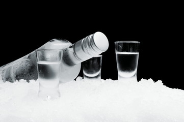 Bottle with glasses of vodka lying on ice on black background