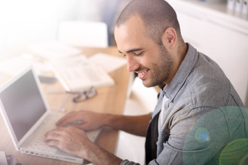 Fototapeta na wymiar Smiling young man in office working on laptop