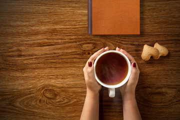 woman with cup of tea, cookies and book on wood