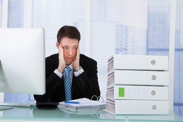 Worried Businessman Looking At Binders On Desk