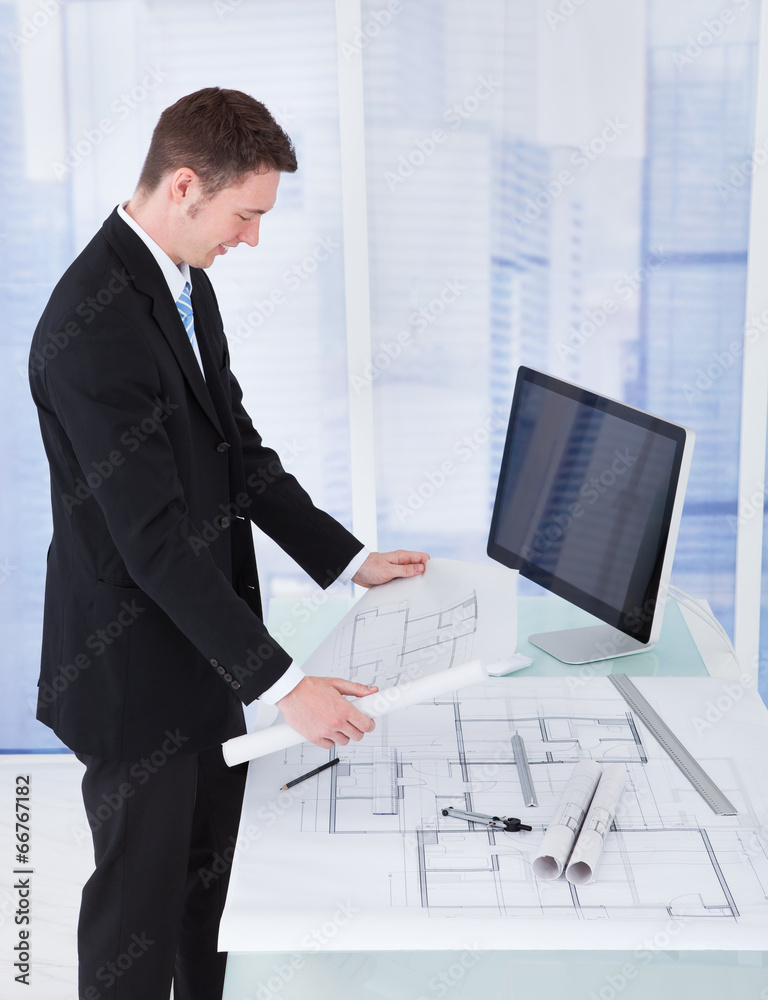 Poster businessman looking at blueprint at computer desk