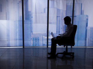 Businessman Using Laptop On Office Chair By Window