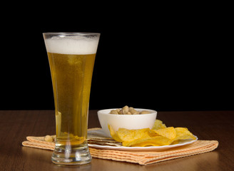 Glass of beer and snack on a black background