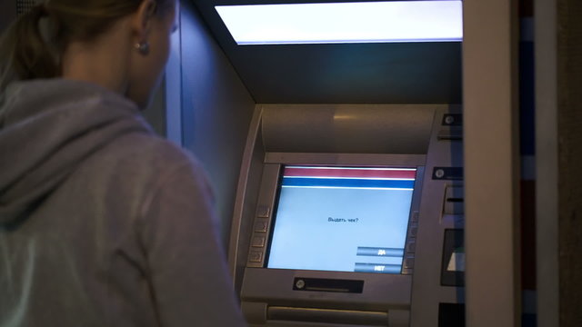 Woman using ATM outdoor in the evening
