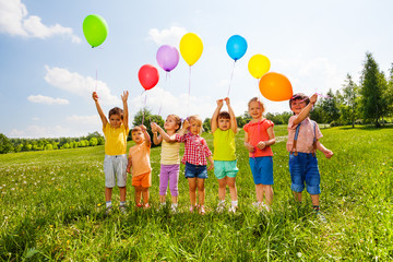 Seven children with balloons in green field