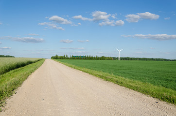Fototapeta na wymiar Rural gravel road near fields and windmill