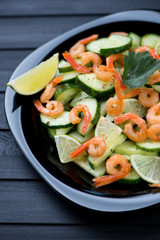 Black plate with shrimp, lime and cucumber salad, vertical shot