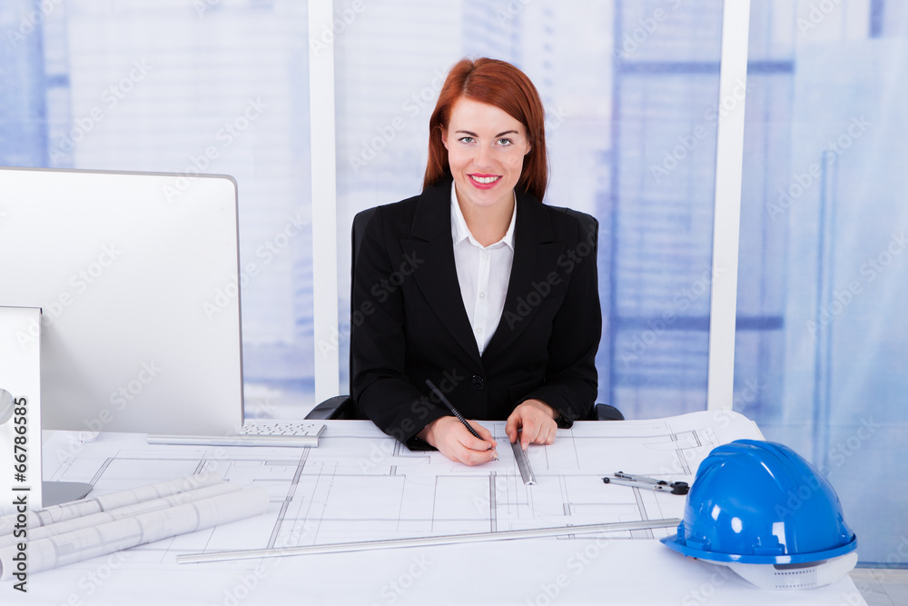 Poster businesswoman using computer with blueprints at desk