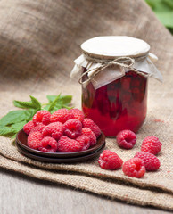 Raspberry preserve in glass jar and fresh raspberries on a plate