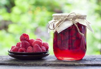 Raspberry preserve in glass jar and fresh raspberries on a plate