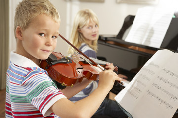 Boy and girl playing violin and piano at home © Monkey Business