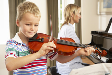 Young boy playing violin accompanied by teacher