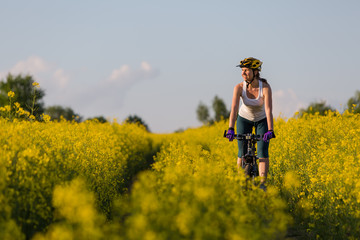 Woman is cycling in yellow rapeseed field