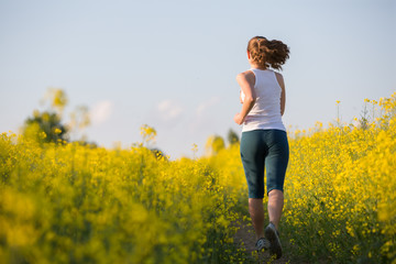 Naklejka na ściany i meble Young woman is jogging in yellow rapeseed field at sunset
