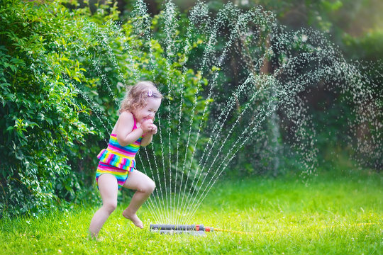 Little girl playing with garden sprinkler