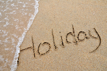 Holiday word written on sandy beach