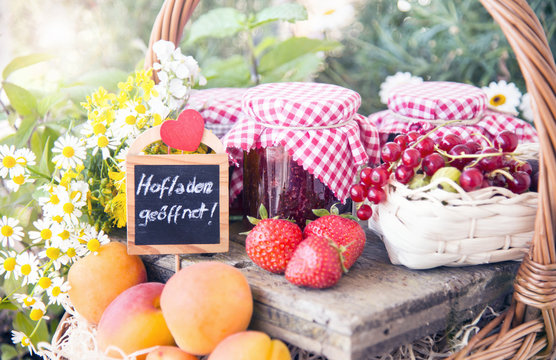 Hofladen geöffnet Kreideschild mit frischem Obst, Beeren und selbstgemachten Marmeladen in einem Korb, dekoriert mit Blumen