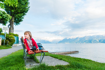 Cute toddler boy resting on a bench next beautiful lake