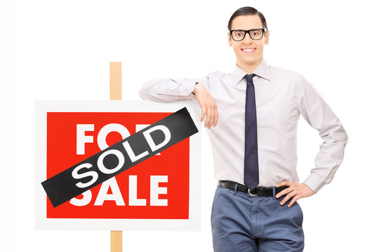 Male real estate agent leaning on a sold sign