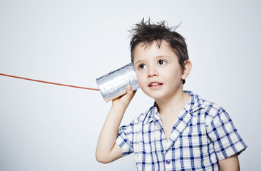 Happy child using a can as telephone against gray background