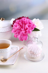 Composition of beautiful peonies in vase, tea in cup and