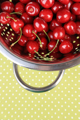 Sweet cherries in colander on color napkin background