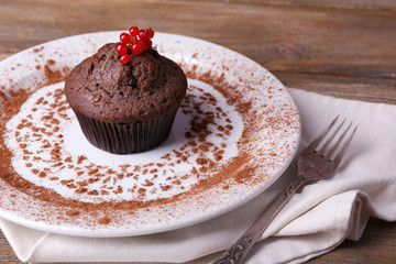 Chocolate muffin with red currant on plate on wooden background