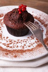 Chocolate muffin with red currant on plate on wooden background