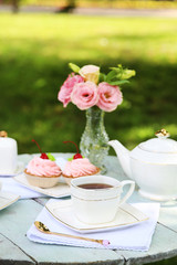 Coffee table with teacups and tasty cakes in garden