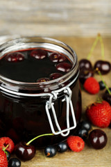 Tasty jam with berries in glass jar on wooden table