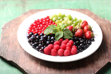 Forest berries on plate, on color wooden background