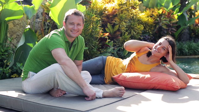 Couple lying on mattress in garden and smiling to the camera