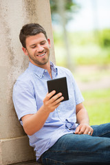 Young man reading E-book outside